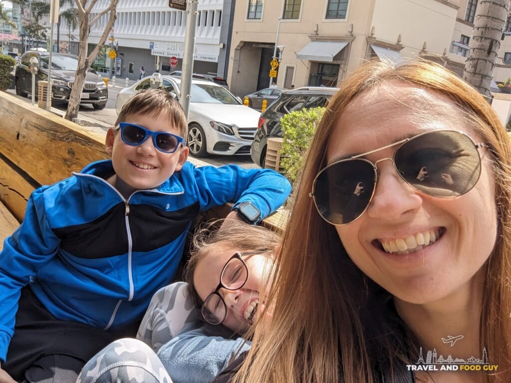 Vika, Josh and Emily smiling in sunglasses on a bench on Wilshire Boulevard in Beverly Hills.