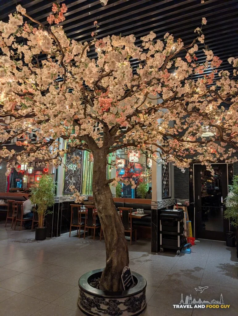 A large artificial cherry blossom tree growing up through the middle of a dining room at Wu's House.
