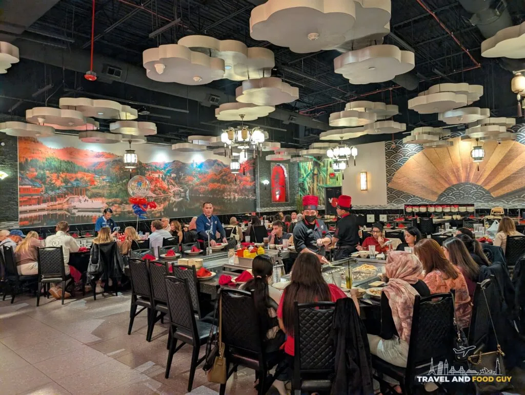 A large dining room at Wu's House full of people at long tables under cloud shaped ceiling lights and a painted mural.