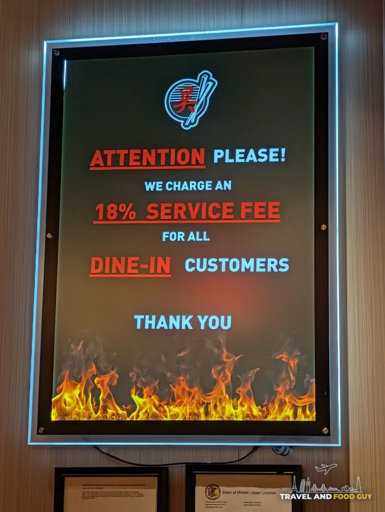 A lit sign at Wu's House Kildeer that reads Attention please, we charge an 18% service fee for all dine-in customers, thank you.